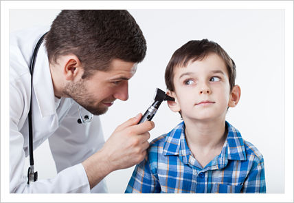 Male Physician is looking in a young boy patient&apos;s ear with an Otoscope