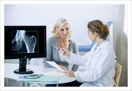 Female Radiologist sitting down next to a female patient and pointing to a screen that is showing an X-Ray