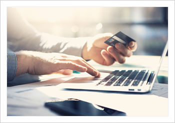 Man is sitting down with an open laptop in front of him and holding a bank card in his other hand